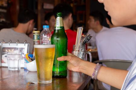 Female hand holding bottle of beer on table in reataurant.の写真素材