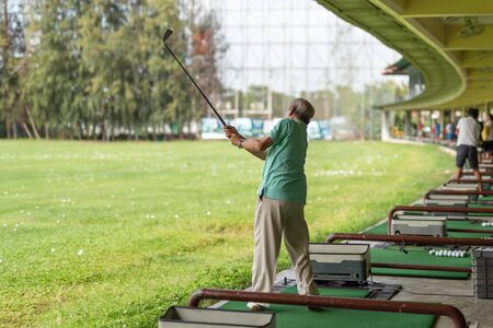 Senior man exercise practicing his golf swing at golf driving range.の写真素材