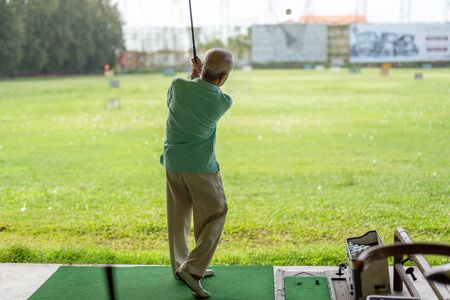 Senior man exercise practicing his golf swing at golf driving range.の写真素材