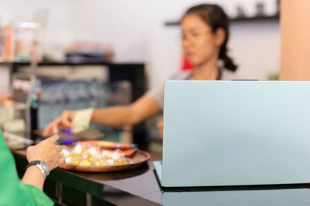 Laptop on top of cafe counter with woman taking money from customer.の写真素材