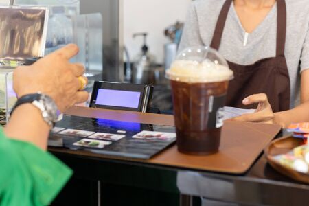 Woman barista serving iced coffee to customer at counter bar in cafe.の写真素材