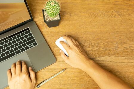 Business man hand using laptop and holding mouse with pen on wooden desk.の写真素材