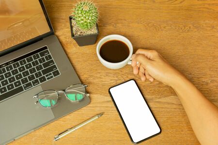 Businessman hand holding coffee cup with laptop and eyeglasson wooden desk.の写真素材
