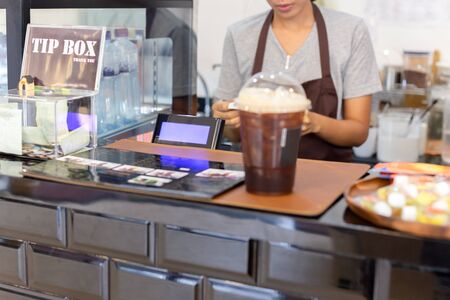 Selected focus cash register with woman barista working behind the counter bar.の写真素材