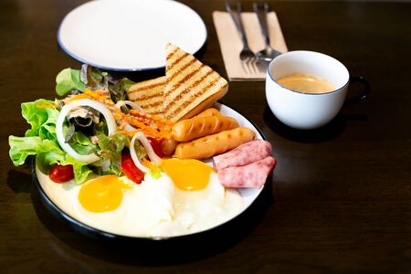 Breakfast set, with vegetable salad, ham, bacon, fried egg, sausage and cup of coffee on table.の写真素材