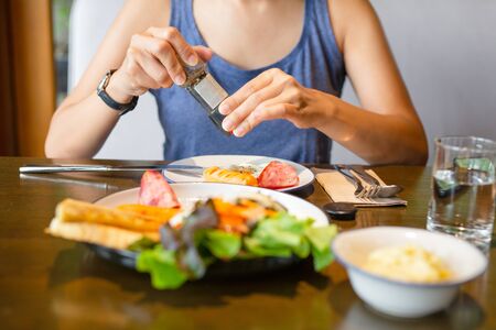 woman grinding pepper over fried eggs at breakfast with glass of water on table.の写真素材