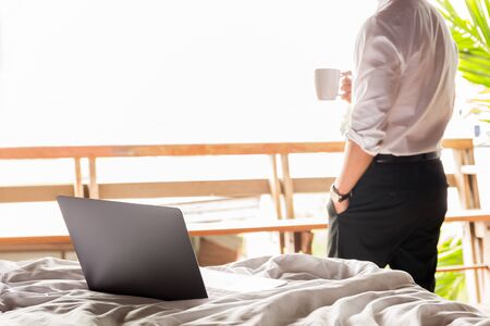 Focus laptop on the bed with businessman holding coffee in cup in background.の写真素材
