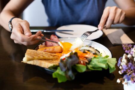 Woman having breakfast with fried eggs, sausages, vegetable and toastの写真素材