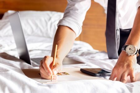 Businessman writing note on paper with laptop on the bed.の写真素材