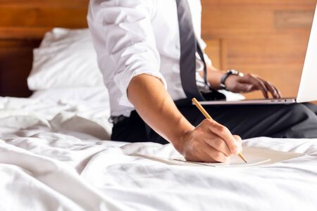 Businessman writing note on paper with laptop on the bed.の写真素材