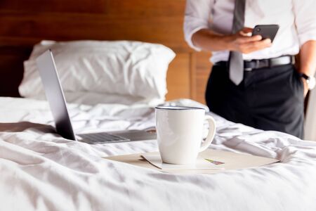 Coffee cup on table with businessman using cell phone and laptop in background.の写真素材
