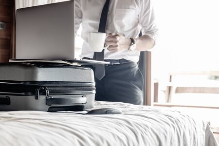 Businessman holding coffee and work on laptop in hotel room on business trip.の写真素材