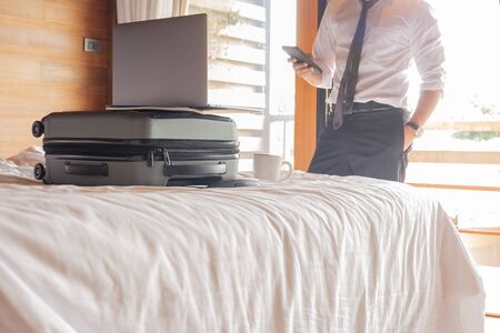 Businessman looking at cell phone with laptop on top of suitcase on the bed.の写真素材