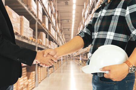 Businessman shaking hands with builder with store factory warehouse in background.の写真素材
