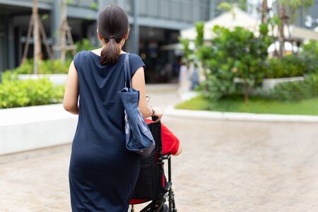 Daughter pushing her mother in wheelchair walking along the shopping mall in open air.の写真素材