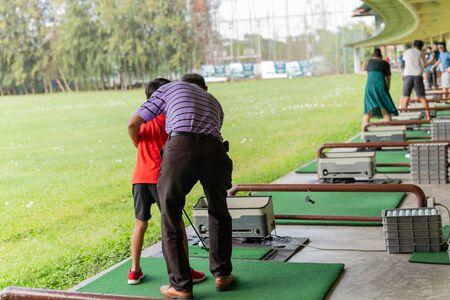 Personal trainer giving lesson to young boy in golf driving range.の写真素材
