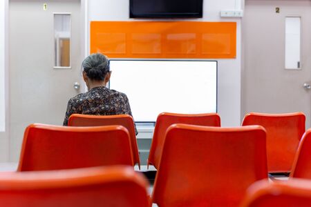 Old woman sit on orange chair waiting for health services in the hospital.