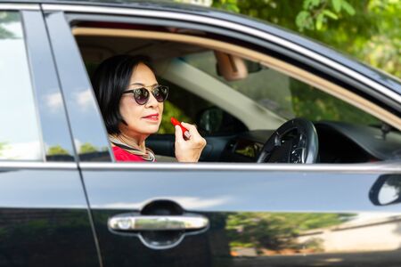 Senior woman with lipstick in her hand sitting in car during a day.の写真素材