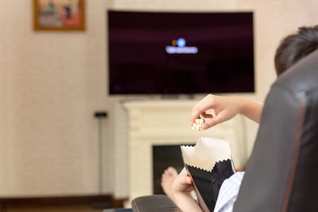 People hand with popcorn watching television at home.の写真素材