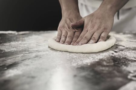 Chef hands knead the dough for pizza preparation.
