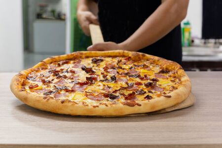Chefs hand holding hawaiian pizza on wooden board.の写真素材