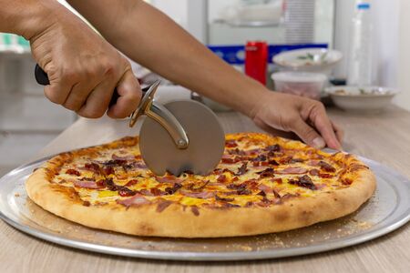 Closeup hand of chef cutting pizza on table.