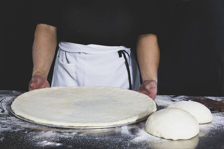 Chef holding uncooked pizza with on table in black backgroundの写真素材