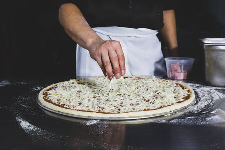 Chefs hand putting cheese on the pizza in black background.の写真素材
