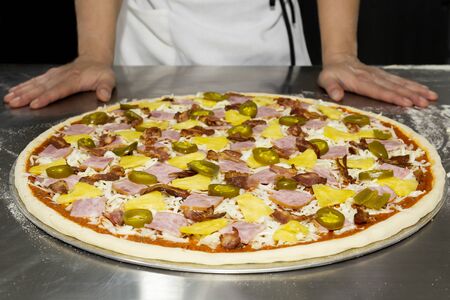 Chefs hand with hawaiian pizza and pineapple, pickled chilli ,ham on the table.の写真素材