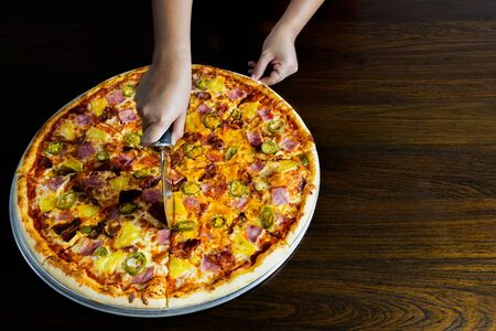 Hand slicing a homemade pizza with pizza cutter on tableの写真素材