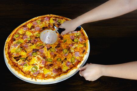 Hand slicing a homemade pizza with pizza cutter on tableの写真素材