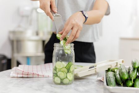 Woman hands with knife putting cucumber into glass jar in kitchen table.の写真素材