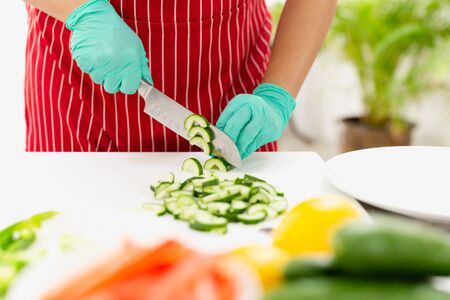 Woman with green glove cutting cucumber in the kitchen on chopping boardの写真素材