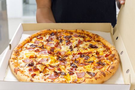 Man holds a open box of pizza in his hands and offers it to others.の写真素材