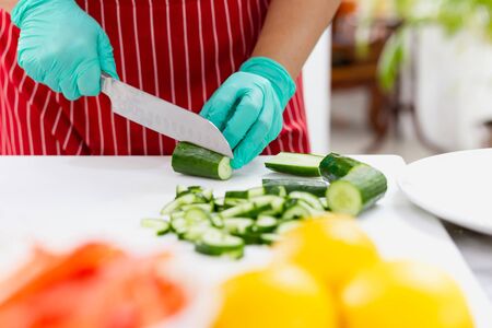 Woman with green glove cutting cucumber in the kitchen on chopping boardの写真素材