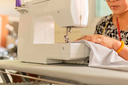 Old women hands stitching fabric on sewing machine at home.の写真素材
