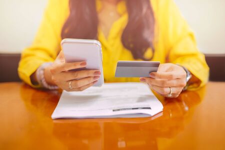 Businesswoman using cell phone banking application paying bills at home.