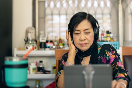 Attractive senior woman listening to music in kitchen at home.