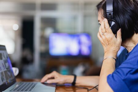 Senior woman with headphones and laptop at home.の写真素材
