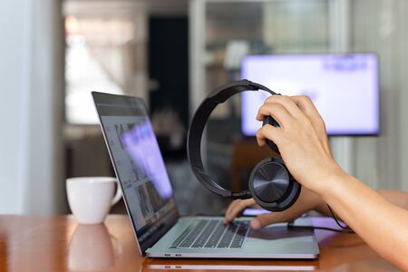 Male hands holding headphones and working on laptop computer at home.