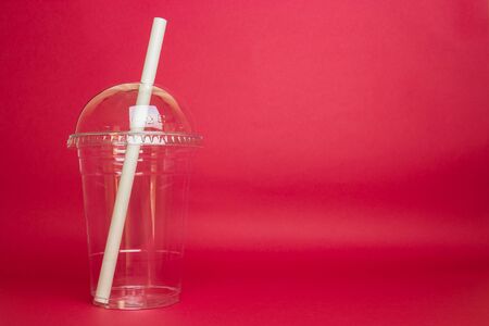 Empty plastic glss with paper straw isolated in red backgroundの写真素材