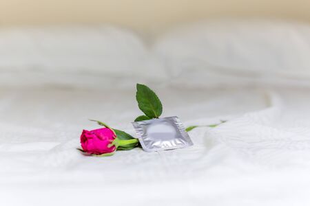 Condom and rose flower on the bed.
