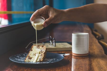 Mans pouring custard cream Into fruit cake with cup of coffee on table.の写真素材