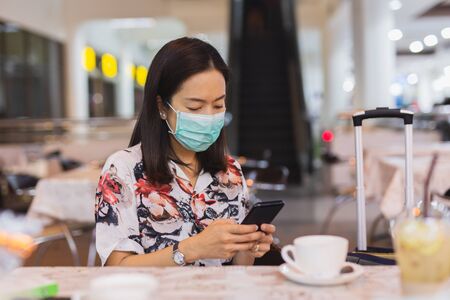 Female passenger at the airport wearing protective mask and using cell phone.