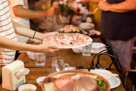Shot in low light hand holding pork slice for hot pan bbq at family dinner.の写真素材