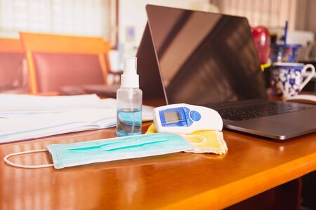 Alcohol spray and thermometer on table with surgical mask virus protection.の写真素材