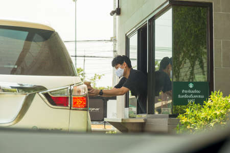 Staff with protective mask serving coffee to customer at drive thru counter.のeditorial素材