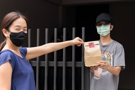 Woman with protective mask delivering food to customer at doorway new normal.の写真素材