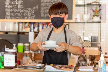 Social distance conceptual small business waiter serving coffee to customer in cafe.の写真素材