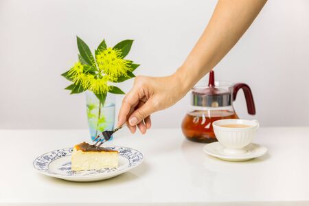 Female hand holding fork eating Basque Burnt Cheesecake with cup of tea on table.の写真素材